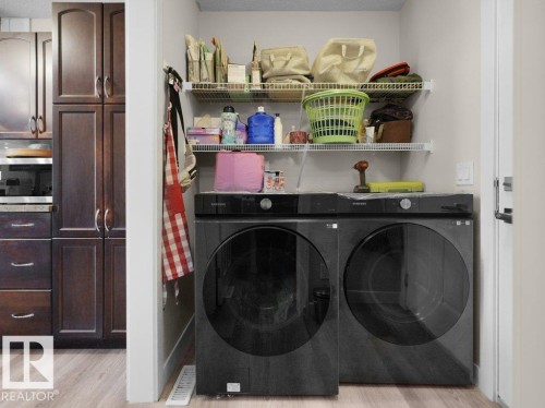 Dedicated laundry area featuring modern black-finish front-load appliances, wire shelving, and wood-finish flooring - 3756 8 Street, Edmonton, AB 