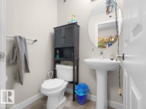 Bathroom featuring a white pedestal sink, circular wall-mounted mirror, and wood-finish flooring - 3756 8 Street, Edmonton, AB 