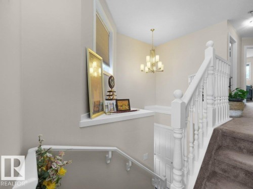 Upper-level landing featuring a brass chandelier, window with blinds, white balustrade, and carpeted stairs - 3756 8 Street, Edmonton, AB 