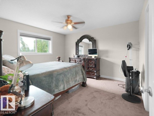 Bedroom featuring a window with exterior tree scenery, light neutral wall paint, ceiling fan with integrated lighting, and carpeted flooring - 3756 8 Street, Edmonton, AB 