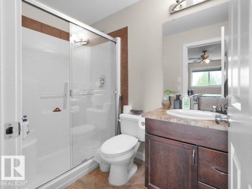 Full bathroom featuring a shower with a sliding glass enclosure, a white toilet, and a vanity with a dark wood-finish cabinet and a light-colored countertop - 3756 8 Street, Edmonton, AB 