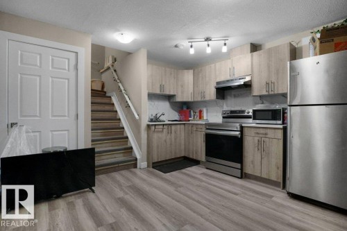 Kitchen area featuring wood-finish cabinetry, stainless steel appliances, laminate wood-look flooring, and a track lighting fixture - 3756 8 Street, Edmonton, AB 