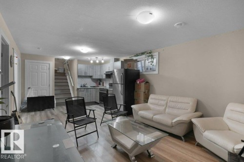 Open-concept living space featuring wood-finish flooring, a contemporary kitchen with stainless steel appliances, light gray cabinetry, and a subway tile backsplash - 3756 8 Street, Edmonton, AB 