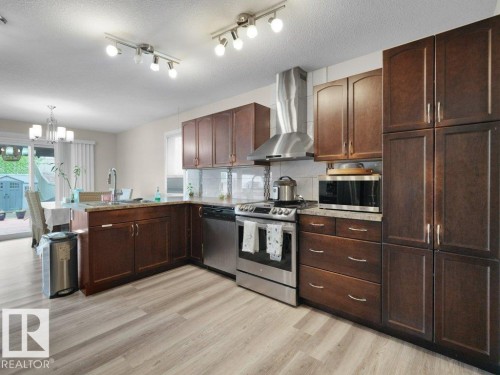 Spacious kitchen featuring wood-finish flooring, dark wood cabinetry, stainless steel appliances including a range and dishwasher, and light-toned countertops - 3756 8 Street, Edmonton, AB 