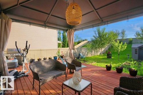 Covered outdoor deck with wood-finish flooring, featuring a woven pendant light fixture and privacy drapes - 3756 8 Street, Edmonton, AB 