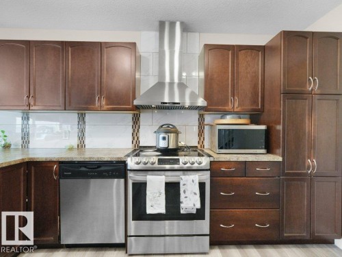 Stainless steel range and matching range hood, brown wood-finish cabinetry, light-toned countertops, tile backsplash, and light wood-finish flooring - 3756 8 Street, Edmonton, AB 