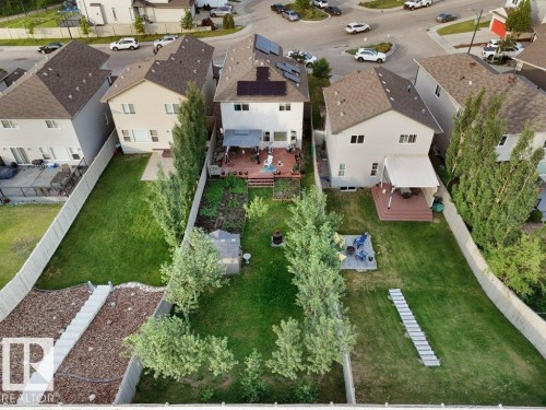 Rear exterior featuring a two-story residence with solar panels, a multi-level wood deck, a covered patio, and a fenced backyard with mature trees and landscaped garden beds - 3756 8 Street, Edmonton, AB 