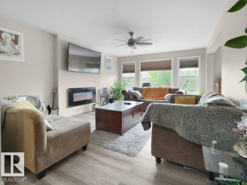 Spacious living area featuring wood-finish flooring, an electric fireplace, and multiple windows with roller blinds - 3756 8 Street, Edmonton, AB 