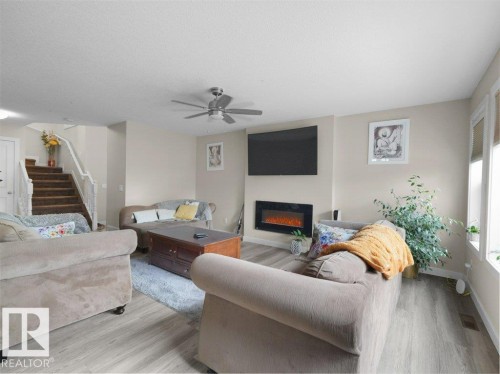 Open-concept living space featuring wood-finish flooring, a contemporary wall-mounted electric fireplace, and a ceiling fan with integrated lighting - 3756 8 Street, Edmonton, AB 