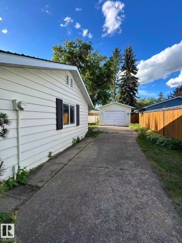 Property exterior featuring light-colored horizontal siding, black window shutters, and a concrete driveway leading to a detached garage - 13112 63 Avenue, Edmonton, AB 