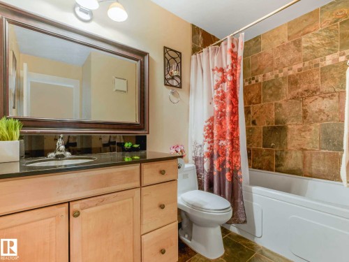Bathroom featuring a light wood-finish vanity with a dark countertop, an integrated sink, and a framed mirror - 403 10165 113 Street, Edmonton, AB 