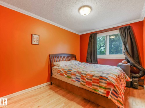 Room featuring bright orange walls, light wood-finish flooring, white baseboards, and crown molding - 403 10165 113 Street, Edmonton, AB 