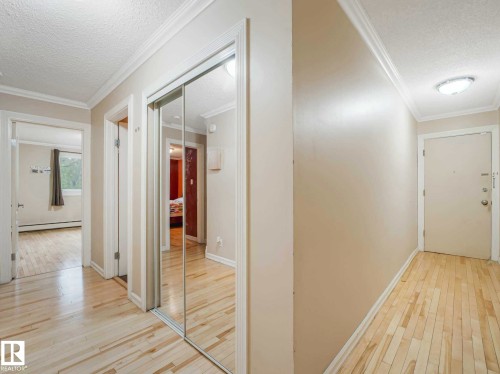 Entryway featuring light wood-finish flooring, crown molding, and mirrored closet doors - 403 10165 113 Street, Edmonton, AB 