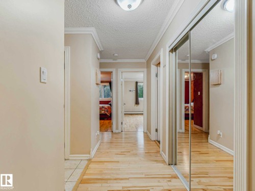 Hallway featuring light wood-finish flooring, white baseboards, and crown molding - 403 10165 113 Street, Edmonton, AB 