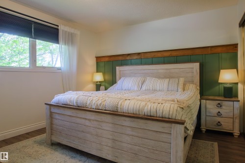 Bedroom featuring a paneled accent wall, wood-finish flooring, and a large window with roller shades and sheer curtains - 58 Lodgepole Crescent, St. Albert, AB 