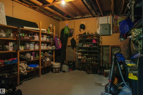 Unfinished basement area featuring exposed ceiling joists, wood shelving units, and a visible electrical service panel - 58 Lodgepole Crescent, St. Albert, AB 