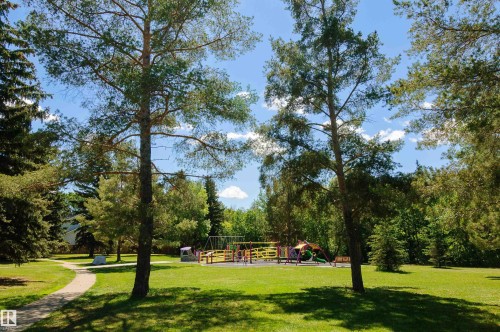Expansive green space featuring a playground with slides and swings, mature trees, and a paved walking path - 58 Lodgepole Crescent, St. Albert, AB 