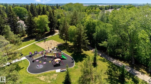 Expansive park area featuring a modern playground with soft-fall surfacing, a swing set on sand, mature trees, and paved walking paths - 58 Lodgepole Crescent, St. Albert, AB 