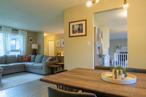 Wood-finish flooring throughout, with an open-concept living area featuring large windows with white sheer curtains - 58 Lodgepole Crescent, St. Albert, AB 