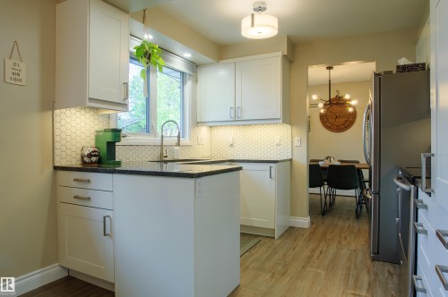 Kitchen featuring white shaker-style cabinetry, dark countertops, a hexagonal tile backsplash, stainless steel appliances, and wood-finish flooring - 58 Lodgepole Crescent, St. Albert, AB 