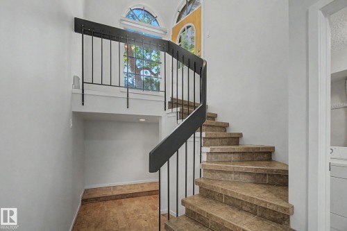 Curved staircase featuring neutral tile steps and black metal railings - 11150 83 Avenue, Edmonton, AB 