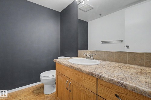 Bathroom featuring a wood-finish vanity with a built-in sink, speckled countertop, and tiled backsplash - 11150 83 Avenue, Edmonton, AB 