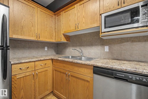 Kitchen featuring wood cabinetry, stainless steel appliances, a double basin sink, laminate countertops, and a tiled backsplash - 11150 83 Avenue, Edmonton, AB 