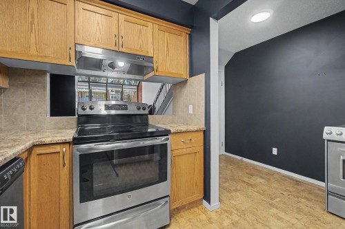 Kitchen featuring wood cabinetry, stainless steel range with overhead hood, and tile backsplash - 11150 83 Avenue, Edmonton, AB 