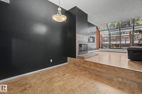 Multi-level living area featuring a prominent fireplace with a tiled surround and hearth, expansive floor-to-ceiling windows, and warm-toned flooring - 11150 83 Avenue, Edmonton, AB 