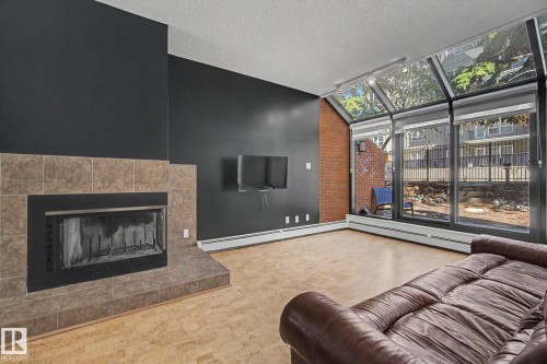 Living area featuring a tiled fireplace with a black metal insert, expansive floor-to-ceiling windows, and wood-finish flooring - 11150 83 Avenue, Edmonton, AB 