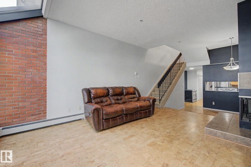 Living room featuring a prominent exposed brick wall, light-toned flooring, and a fireplace with a tiled hearth and surround - 11150 83 Avenue, Edmonton, AB 