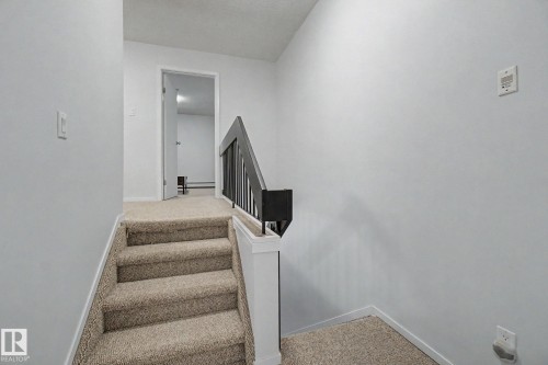 Carpeted staircase with dark railing leading to an upper landing - 11150 83 Avenue, Edmonton, AB 