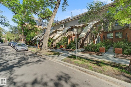 Multi-level townhome featuring a brick facade with arched entryway, exterior staircase, and mature tree landscaping - 11150 83 Avenue, Edmonton, AB 