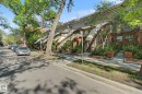 Multi-level townhome featuring a brick facade with arched entryway, exterior staircase, and mature tree landscaping - 11150 83 Avenue, Edmonton, AB 