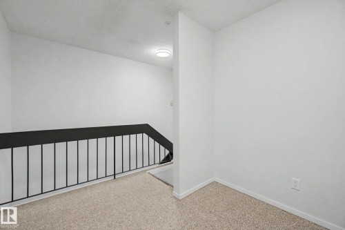 Interior landing featuring a contemporary black metal railing and textured light-toned carpeting - 11150 83 Avenue, Edmonton, AB 