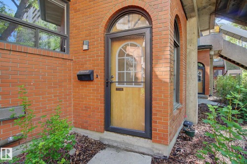 Brick facade with an arched entry door featuring decorative glass, a storm door, and a wall-mounted mailbox - 11150 83 Avenue, Edmonton, AB 