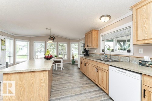 Spacious kitchen featuring an island, extensive cabinetry, wood-finish flooring, ample natural light from multiple windows, and a built-in dishwasher - 233 Oak Wood Drive, Edmonton, AB 