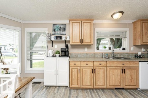 Kitchen featuring wood-finish flooring, light wood cabinetry with dark hardware, a double basin sink, and a tiled backsplash - 233 Oak Wood Drive, Edmonton, AB 