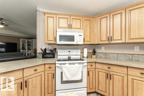Kitchen featuring wood-finish cabinetry with black hardware, complementing countertops, a tile backsplash, and built-in microwave - 233 Oak Wood Drive, Edmonton, AB 