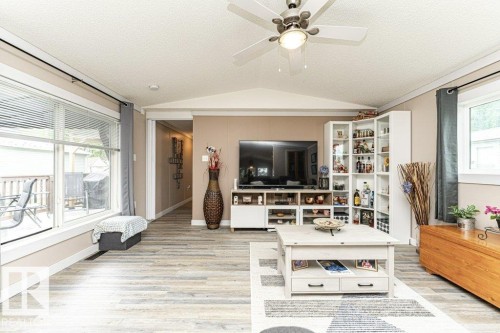 Open-concept living space with wood-finish flooring, a ceiling fan with integrated lighting, and multiple windows - 233 Oak Wood Drive, Edmonton, AB 