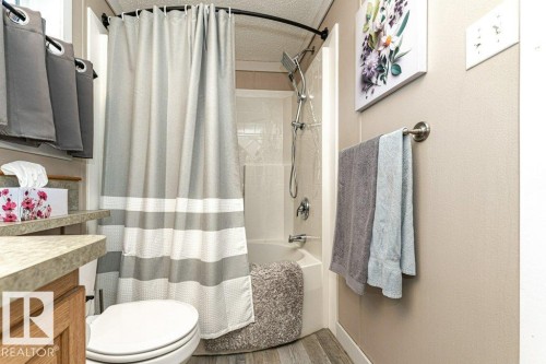 Bathroom featuring a tub/shower combination with a curved shower rod, wood-finish flooring, a toilet, and a vanity with a laminate countertop and wood-finish cabinetry - 233 Oak Wood Drive, Edmonton, AB 