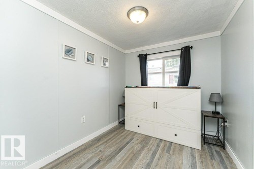 Room featuring wood-finish flooring, light blue panel walls, white crown molding, and a white ceiling with a flush-mount light fixture - 233 Oak Wood Drive, Edmonton, AB 