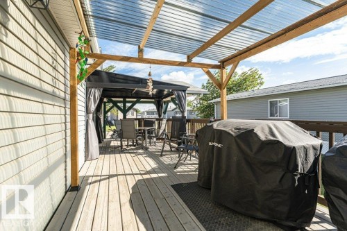 Expansive outdoor deck featuring wood-finish flooring, a clear corrugated roof, and a freestanding pergola with fabric curtains - 233 Oak Wood Drive, Edmonton, AB 