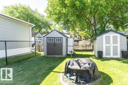 Expansive backyard featuring two storage sheds with shingled roofs and paneled siding, a manicured lawn, and mature trees providing natural shading - 233 Oak Wood Drive, Edmonton, AB 