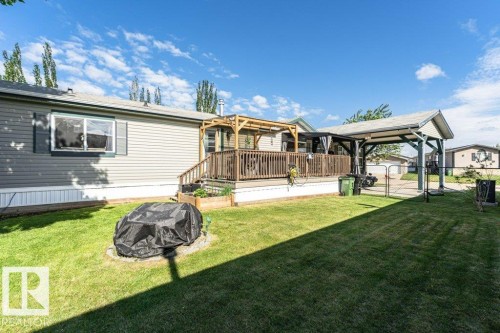Expansive backyard featuring a green lawn, wood deck, carport, and a raised garden bed - 233 Oak Wood Drive, Edmonton, AB 