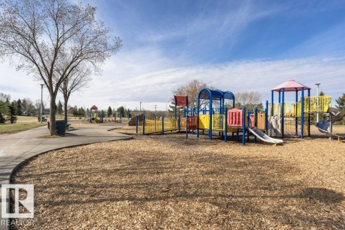 Playground area featuring multi-colored play structures with slides, climbing elements, and protective ground cover - 233 Oak Wood Drive, Edmonton, AB 
