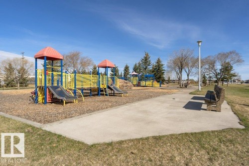 Community park area featuring a modern playground structure with slides and climbing elements set on a wood chip surface - 233 Oak Wood Drive, Edmonton, AB 