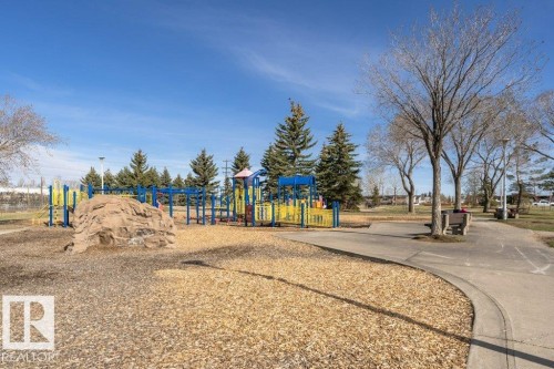 Park area featuring a large playground with blue and yellow equipment, a rock-climbing structure, and a wood chip surface - 233 Oak Wood Drive, Edmonton, AB 