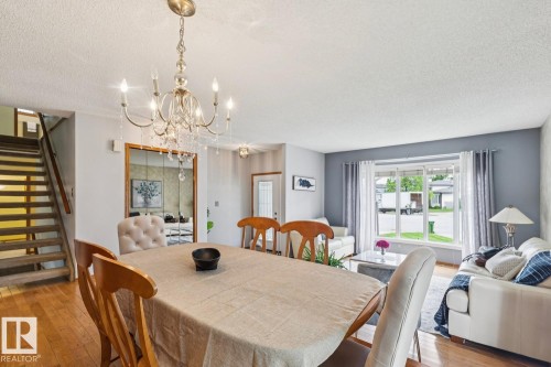 Open-concept living area featuring wood-finish flooring, a crystal chandelier, and a prominent front-facing window - 15804 80 Street, Edmonton, AB 