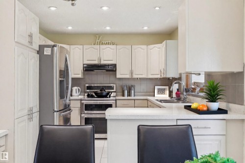 Bright kitchen featuring white cabinetry, integrated stainless steel appliances, recessed ceiling lighting, a tile backsplash, and a light-toned countertop - 15804 80 Street, Edmonton, AB 